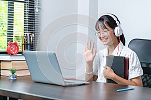 Happy smiling female student wearing headphones talking in online discussion meeting using laptop in home office. female college