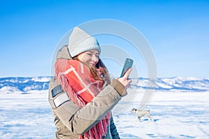 Happy smiling female wonderer dressed in warm winter clothes online chatting in mobile phone