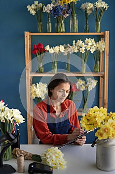 Happy smiling florist woman with clipboard writing and making notes order working in her flower shop. People, business