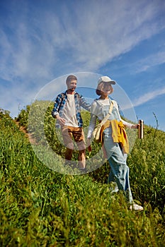 Happy, smiling friends, couple, young man and woman in casual clothes going hiking, walking down the hill on warm summer
