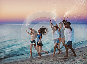 Happy smiling friends running at the beach with sparkling candles