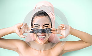 Happy smiling girl applying facial charcoal mask portrait - Young woman having skin care cleanser spa day photo