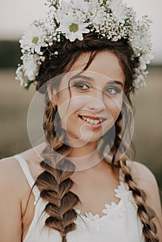 Happy smiling girl with braids and floral wreath in white dress in boho style in summer outdoors