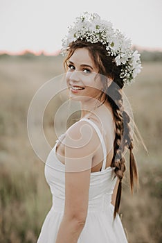 Happy smiling girl with braids and floral wreath in white dress in boho style in summer outdoors