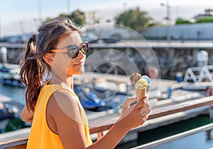 Happy, smiling girl holding ice cream cone with colorful ice cream balls. Sunny sea coastline at the background