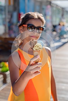 Happy, smiling girl holding ice cream cone with colorful ice cream balls. Sunny sea coastline at the background