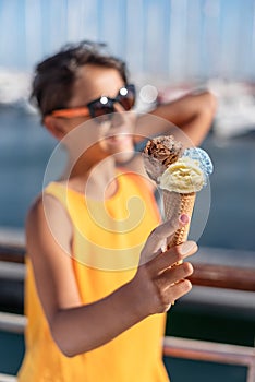 Happy, smiling girl holding ice cream cone with colorful ice cream balls. Sunny sea coastline at the background