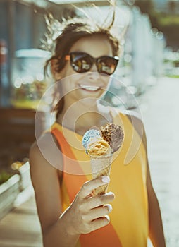 Happy, smiling girl holding ice cream cone with colorful ice cream balls. Sunny sea coastline at the background