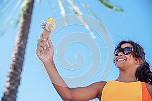 Happy, smiling girl holding ice cream cone with colorful ice cream balls. Sunny sea coastline at the background