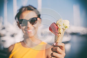 Happy, smiling girl holding ice cream cone with colorful ice cream balls. Sunny sea coastline at the background