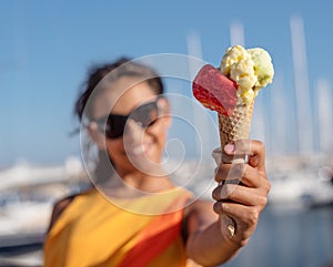 Happy, smiling girl holding ice cream cone with colorful ice cream balls. Sunny sea coastline at the background