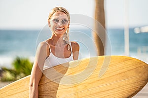 Happy smiling girl holding a surfboar on the coast. Summer island vibes. Watersports. Hobby