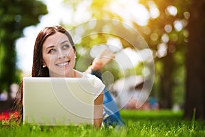 Happy smiling girl laying on grass with laptop