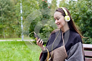 Young happy woman listening music from smartphone with headphones in a quiet Park