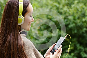 Young happy woman listening music from smartphone with headphones in a quiet Park