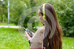 Young happy woman listening music from smartphone with headphones in a quiet Park