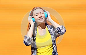 Happy smiling girl listens and enjoys the good music in headphones against colorful orange