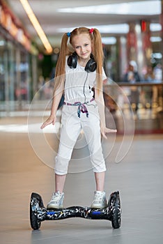 Happy and smiling girl rides on mini segway in the headphones at trading mall. Teenager riding on hover board or gyroscooter and l
