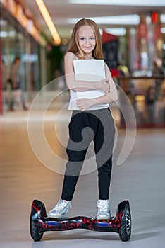 Happy and smiling girl rides on mini segway at trading mall. Teenager riding on hover board or gyroscooter and holding blank sheet