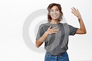 Happy smiling girl saying hello, waving hand, greeting, naming herself, introducing, standing over white background