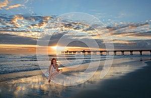 Happy smiling girl with seashells on beautiful beach at sunrise.