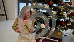 Happy Smiling Girl Standing in Front of Christmas Tree with Gift