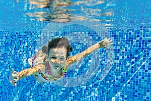 Happy smiling girl swims underwater in pool