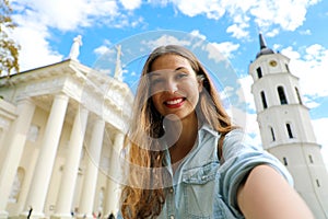 Happy smiling girl taking selfie picture in front of Vilnius Cathedral, Lithuania. Beautiful young woman traveling in Europe