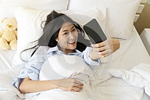 Happy smiling girl using smart phone for selfie on the bed. Beautiful young woman self-portrait with mobile camera lying