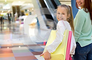 Happy smiling girl walking along the shopping mall with her mother and shopping bags