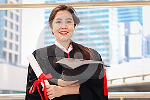 Happy smiling graduated student, young beautiful Asian woman holding square academic hat cap and certificate, standing with arms
