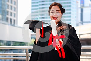 Happy smiling graduated student, young beautiful Asian woman holding square academic hat cap and giving certificate to camera,