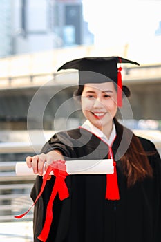 Happy smiling graduated student, young beautiful Asian woman warming square academic hat cap and giving certificate to camera,