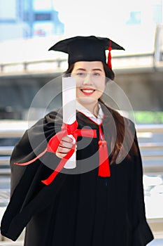 Happy smiling graduated student, young beautiful Asian woman warming square academic hat cap and giving certificate to camera,