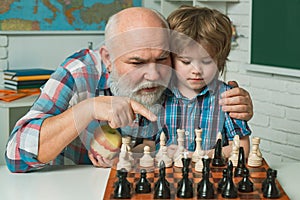 Happy smiling grandson boy with granddad playing chess together. Happy family. Two men generation, grandfather father