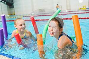 Happy and smiling group of children learning to swim with pool noodle