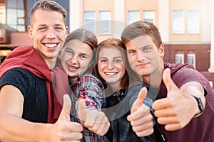 Happy smiling group of students giving thumbs up near university on background