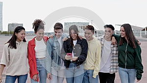 Happy smiling group of young friends holding mobile phone outdoors