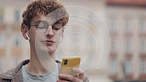Happy smiling hipster guy with glasses chatting with friends at social networks and listen music, using modern