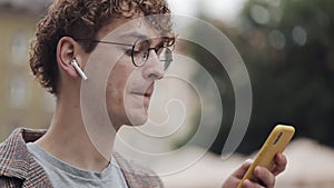 Happy smiling hipster guy with glasses chatting with friends at social networks and listen music, using modern