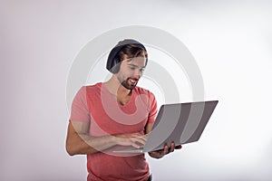 Happy smiling hipster guy with wireless headphone playing games on laptop computer