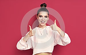 Happy smiling hipster woman showing thumbs up on pink background