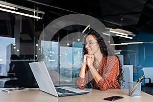 Happy and smiling hispanic businesswoman typing on laptop, office worker with curly hair and glasses happy with