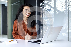 Happy and smiling hispanic businesswoman typing on laptop, office worker with curly hair happy with achievement results