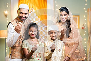 Happy smiling indian couple with kid wishing for ramadan festival by saying hand gesture while looking at camera at home