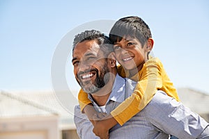 Happy smiling indian father giving son ride on back