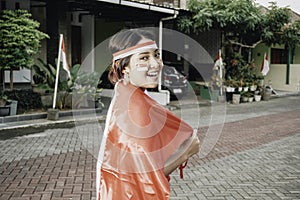 Happy smiling Indonesian woman wearing red kebaya holding Indonesia's flag to celebrate Indonesia Independence Day.