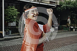 Happy smiling Indonesian woman wearing red kebaya holding Indonesia's flag to celebrate Indonesia Independence Day.
