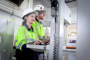 Happy smiling industrial woman and man workers wear helmet and safety vest work together with computer controller, operate