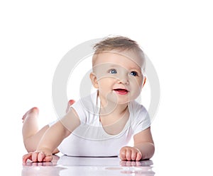 Happy smiling infant child baby boy toddler with blue eyes in white t-shirt is lying on his stomach crawling on white